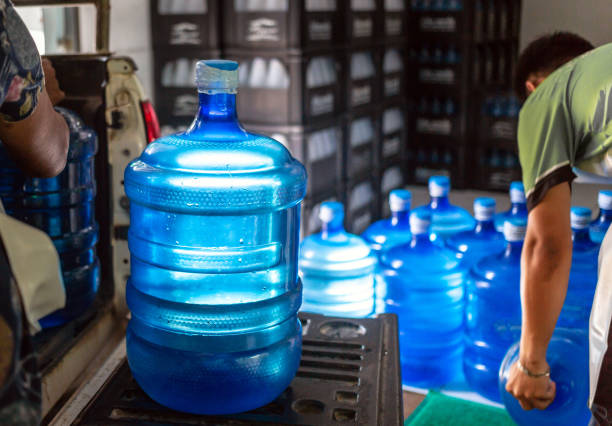 Workers lift gallons of blue drinking water and bottles in crates into the back of a transport truck.